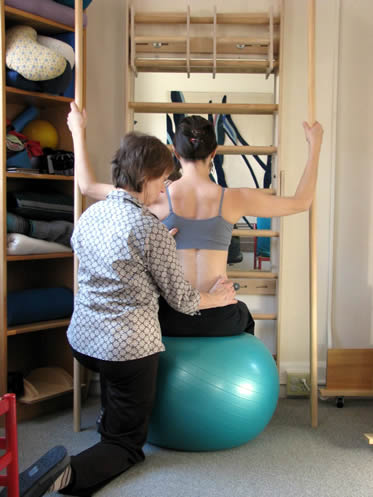 Exercise on gymnastic ball with poles to stabilize spine in mid line 